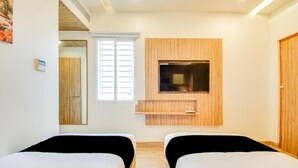 A hotel room with two beds, a wooden wall panel, a window, and a mirror. - Inn The Centre (Nellore)