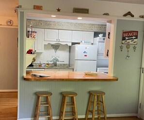 A kitchen with white cabinets, a wooden countertop, and a refrigerator. There are three wooden stools in front of the counter. - E13 Build family memories,  comfortable, clean (St. Simons Island)