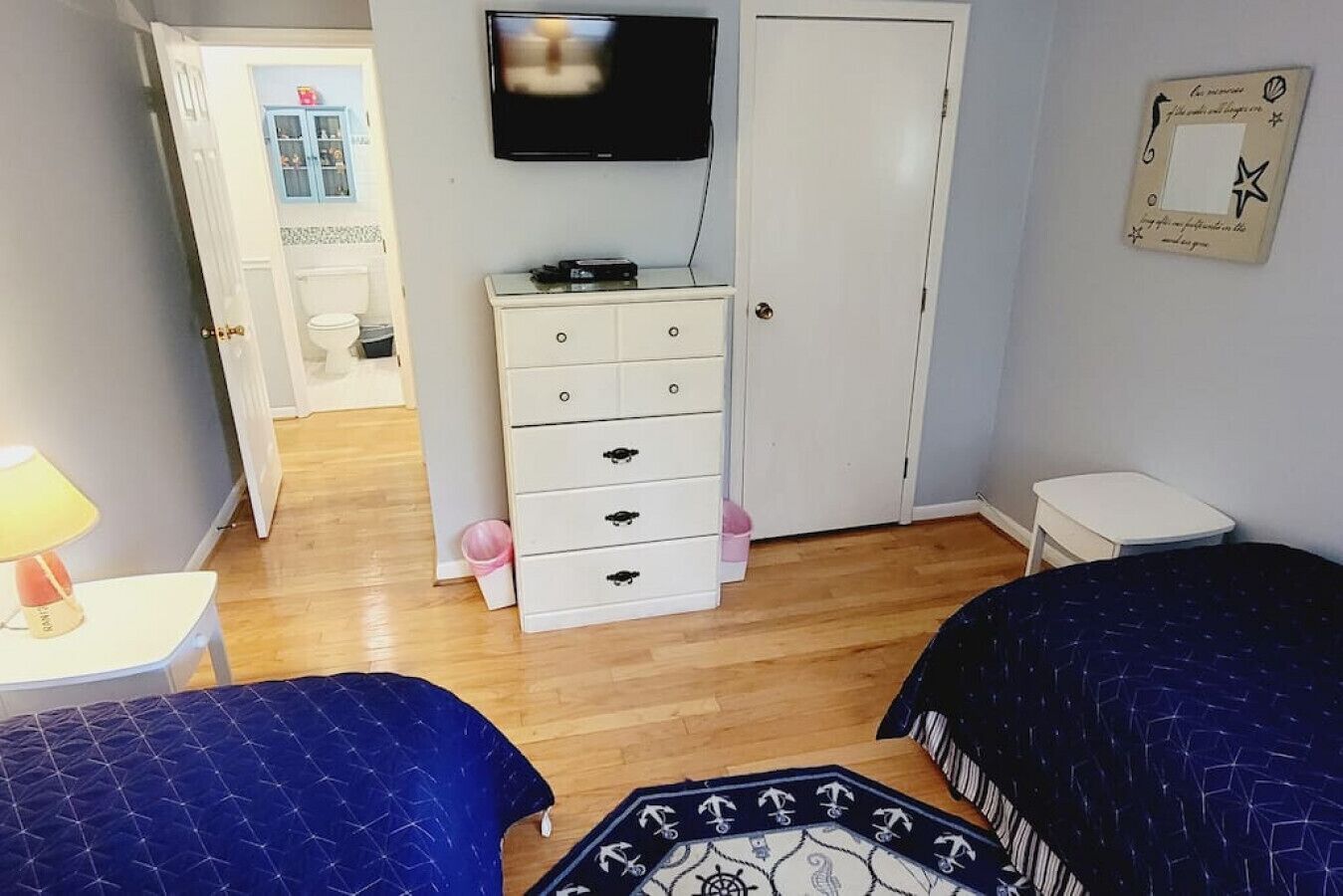 Quarto com duas camas, uma cômoda, televisão e uma mesinha com abajur.