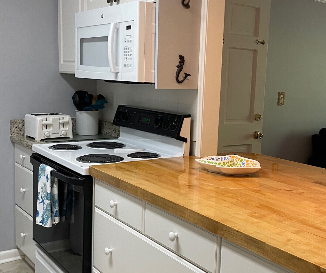 A kitchen with a stove, microwave, toaster, and a wooden countertop.