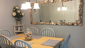 A dining area with a wooden table, six chairs, a mirror with a seashell frame, and a vase with flowers. - E13 Build family memories,  comfortable, clean (St. Simons Island)