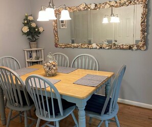 A dining area with a wooden table, six chairs, a vase of flowers, a decorative mirror, and wall-mounted lights.