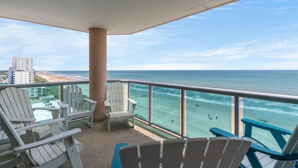 Un balcon avec des fauteuils Adirondack blancs, une vue sur l’océan et une plage en arrière-plan.