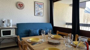 A dining area with a wooden table set for four, a blue sofa, a microwave, and a poster on the wall.