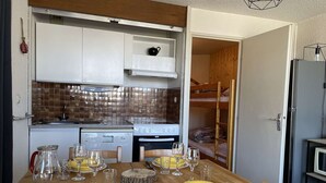 A compact kitchen with white cabinets, a stove, and a microwave. A dining table with yellow plates and glasses is set for four.