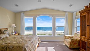 A bedroom with a large bed, a chair, a wooden cabinet, and a view of the beach. - "Sundance" - Oceanfront Home w/ Private Pool, 5 Bedrooms / 4.5 Bathrooms (Holden Beach)
