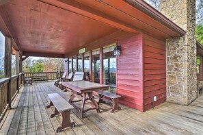 A wooden deck with picnic tables and chairs, a stone wall, and a covered area with a red roof. - Smoky Mountain Retreat w/ Hot Tub, Arcade Games (Pigeon Forge)