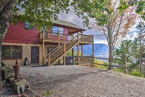 A two-story house with a wooden balcony, a stone foundation, and a view of mountains. - Smoky Mountain Retreat w/ Hot Tub, Arcade Games (Pigeon Forge)