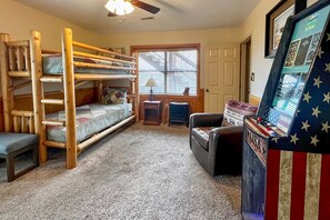 A room with a bunk bed, a small table with a lamp, a vintage arcade machine, and a door leading outside. - Smoky Mountain Retreat w/ Hot Tub, Arcade Games (Pigeon Forge)