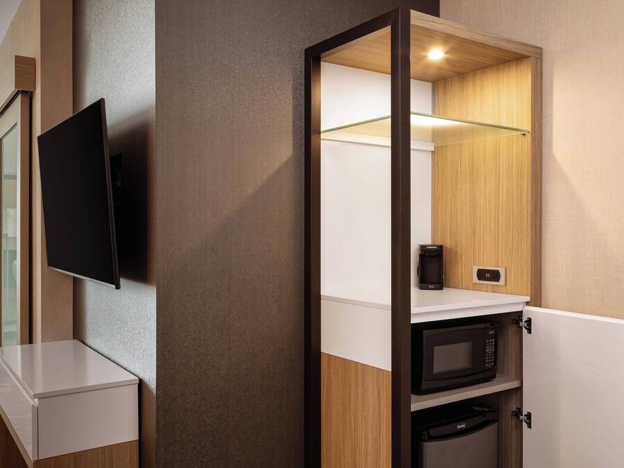 Habitació d'hotel compacta amb televisió de pantalla plana penjada a la paret, microones i una petita cafetera a una estant.