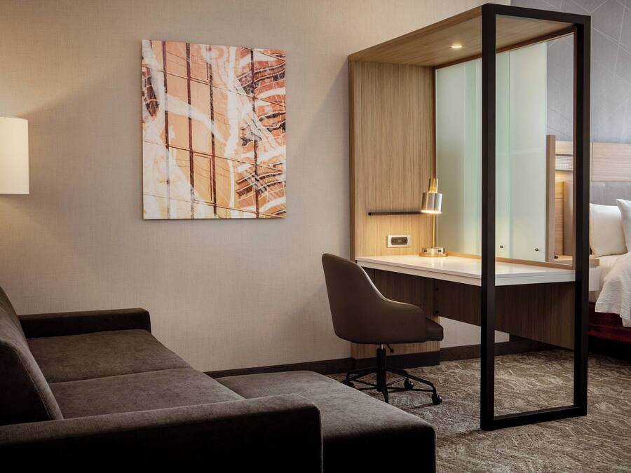 Habitación de hotel con sofá, escritorio, silla, cama y un espejo grande.