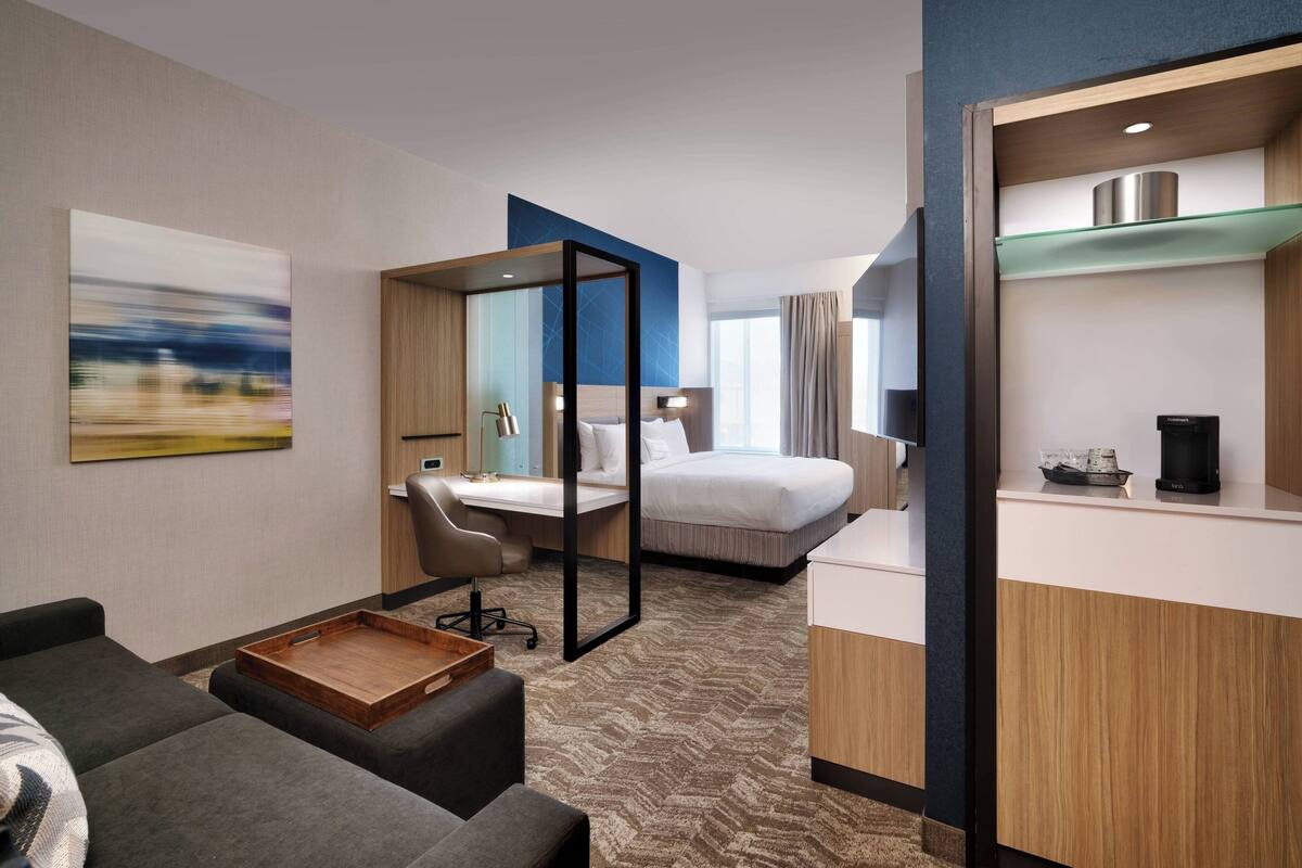 Une chambre d’hôtel avec un lit, un bureau, une chaise, une petite table et une grande fenêtre.