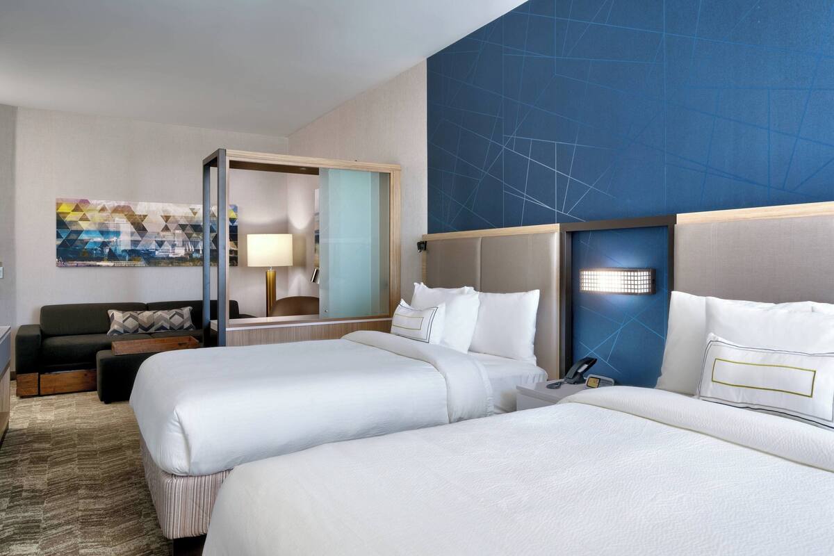 Une chambre d’hôtel avec deux lits, un canapé, un bureau et une grande fenêtre.