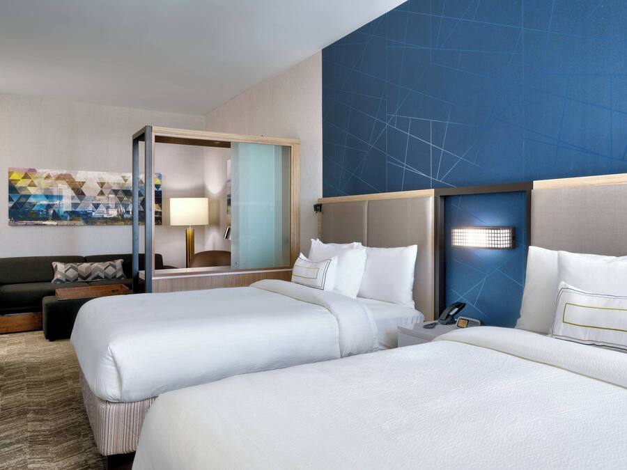 A hotel room with two beds, a sofa, a desk, and a large window.