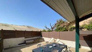 An outdoor patio with a table set for dining, surrounded by chairs, and a covered area with a view of the beach. - Patio Villa 20m from the beach with terrace and parking (Capbreton)
