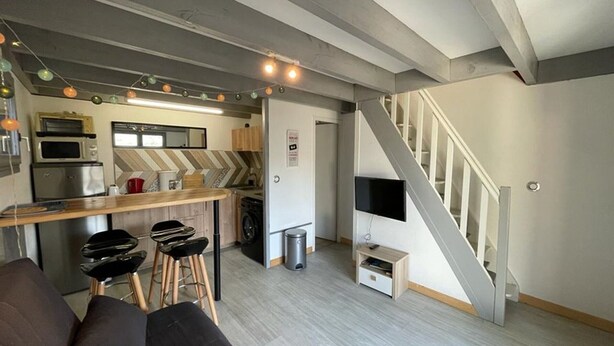 A compact living space with a kitchenette, a sofa, a TV, and a staircase. - Patio Villa 20m from the beach with terrace and parking (Capbreton)