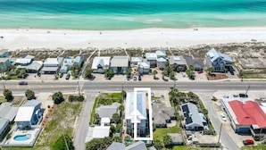 An aerial view of a coastal residential area with houses along the beach, a road, and a clear view of the ocean. - 🌺 Aloha Beaches Gulf-Front Retreat, Pool, Steps to Beach, Sleeps 14 (Panama City Beach)