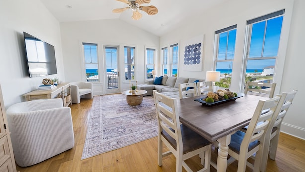 A spacious living room with a large window overlooking the ocean, a dining area with a wooden table and chairs, and a cozy seating area with a sofa and armchairs. - 🌺 Aloha Beaches Gulf-Front Retreat, Pool, Steps to Beach, Sleeps 14 (Panama City Beach)
