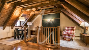 A wooden-floored room with a staircase, a dining table, and a plaid armchair. - Casa Eth Gauèc (Betrén)