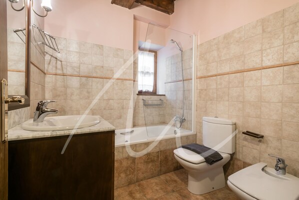 Casa de banho com lavatório, sanita, banheira e chuveiro.