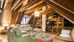 An attic living room with wooden beams, a sofa, a television, and built-in bookshelves. - Casa Eth Gauèc (Betrén)