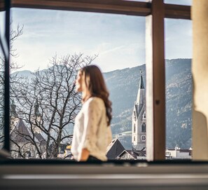 A person standing by a window overlooking a mountainous landscape with a church. - Design Holiday Apartment "901" with Balcony in Central Location (Brixen)