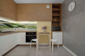 A modern kitchen with wooden cabinets, a microwave, a sink, and two white stools.