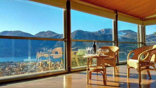 A room with large windows offering a view of a mountainous landscape and a distant city. - Villa Ornella - Luxury Mansion (12 people version) (Mandello del Lario, Province of Lecco, Italy)