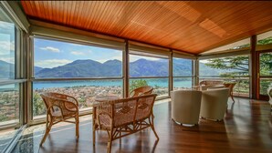 A spacious room with large windows offering a panoramic view of a coastal town and mountains. - Villa Ornella - Luxury Mansion (12 people version) (Mandello del Lario, Province of Lecco, Italy)