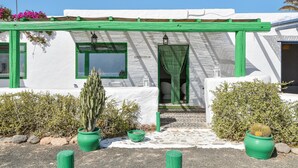Een wit gebouw met groene accenten, een overdekte ingang en bloempotten.