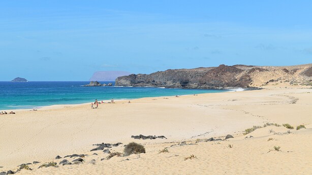 Een strand met helderblauw water, een zandstrand en rotsklippen.