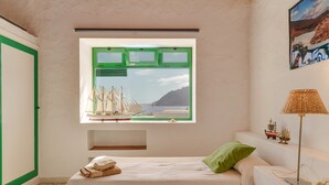 Een slaapkamer met een bed, een raam met uitzicht op boten, een lamp en een klein plankje met spullen.