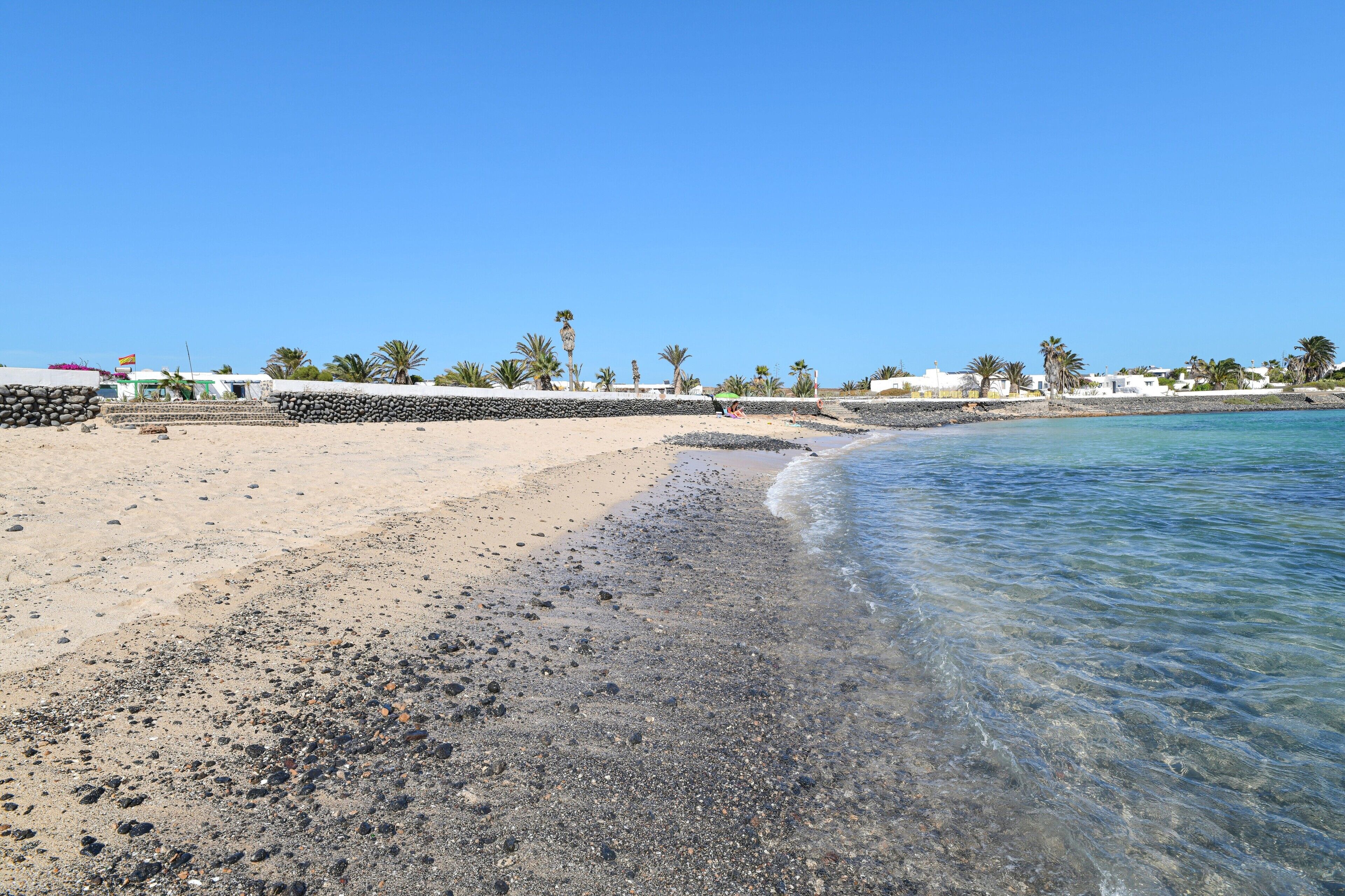 A beach with clear water, pebbles, and palm trees.