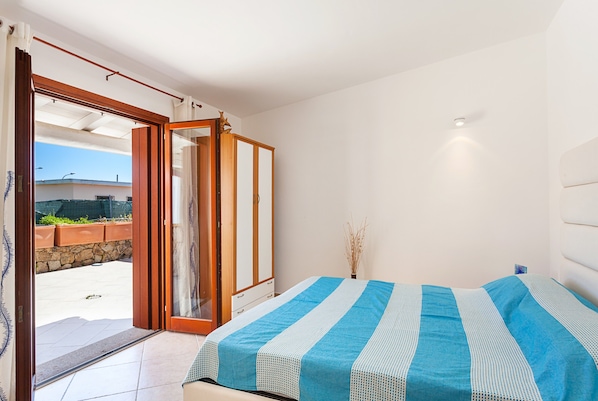 A bedroom with a bed, a sliding door to a balcony, and a view of the outside.