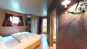 Une chambre à coucher avec un lit, une fenêtre avec des rideaux, un luminaire fixé au mur et une porte donnant sur une autre pièce.