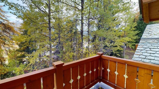 Un balcon en bois offrant une vue sur une zone boisée et, au loin, sur une montagne.