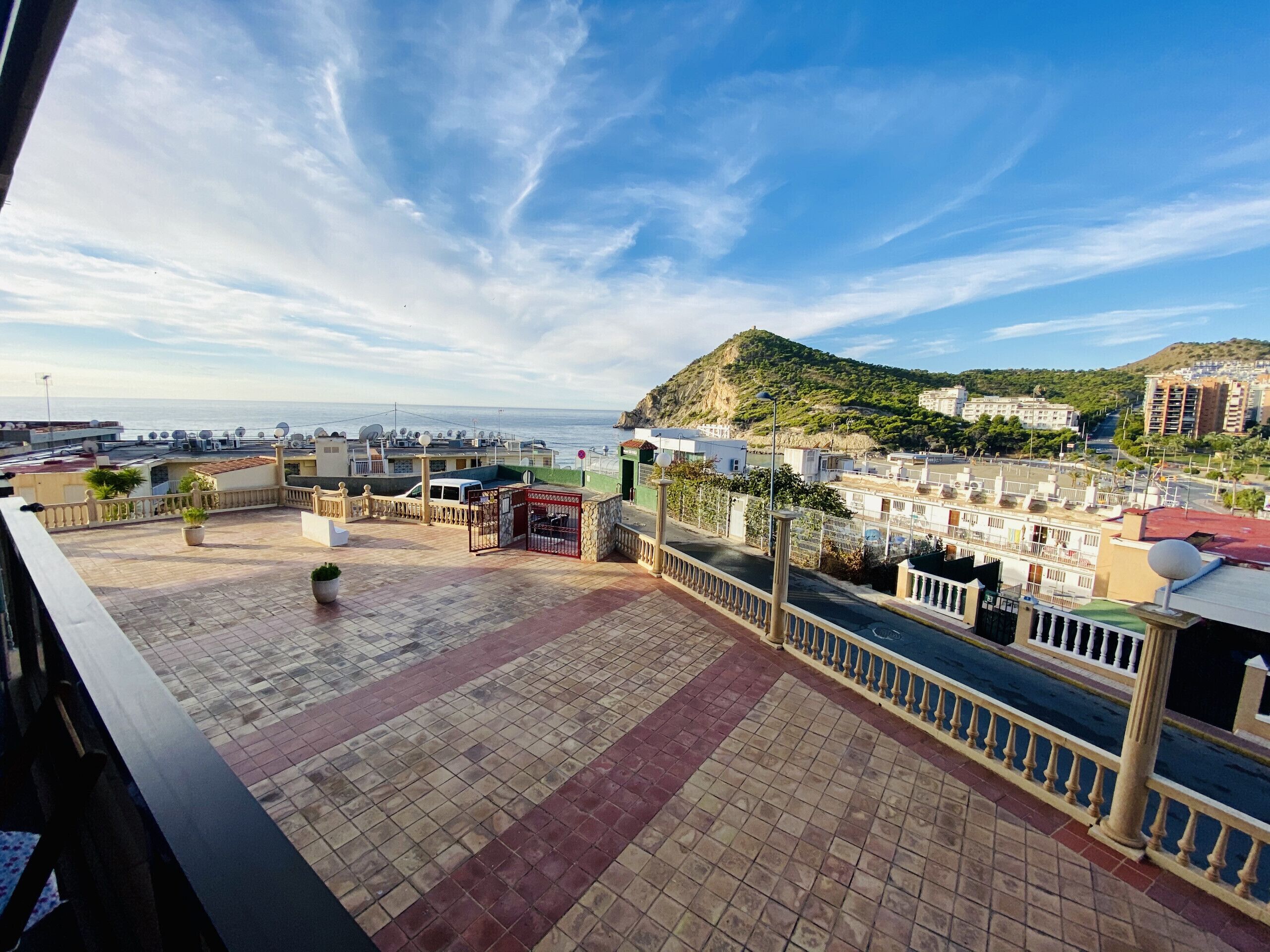 A rooftop terrace with a view of the sea and a hill.