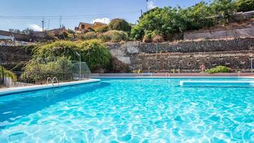 Uma piscina azul cristalina com parede de pedra e vegetação ao fundo.
