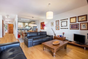 A spacious living area with a sofa, coffee table, and TV, connected to a kitchen with a dining area.