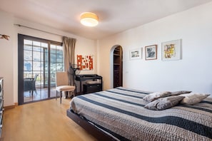 A bedroom with a bed, a desk, a chair, and a view through a large window.