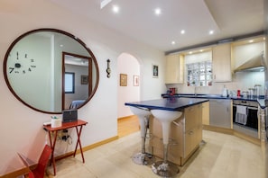 A modern kitchen with a central island, bar stools, and a round mirror on the wall.