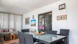 Un comedor con una mesa de vidrio y sillas de mimbre, un sofá con cojines, una mesita de madera y una ventana con cortinas.
