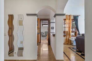 Un couloir avec un miroir aux reflets ondulants, une porte et une vue sur un salon avec un canapé et des rideaux.