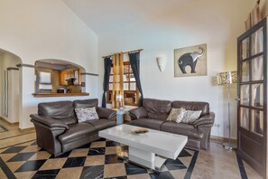 Ein Wohnzimmer mit zwei Ledersofas, einem weißen Couchtisch und einem großen Fenster mit Vorhängen.