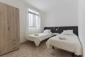 Une chambre avec deux lits, une armoire, une fenêtre avec des rideaux et un sol carrelé.