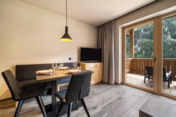 Un espace repas moderne avec une table dressée pour deux personnes, un téléviseur et une vue sur une terrasse en bois et une forêt.
