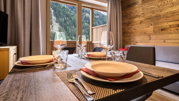 Una mesa de comedor preparada con platos, vasos y cubiertos, un sofá y una pared de madera con vista a una ventana.