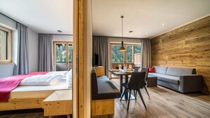 Una habitación moderna con una cama, un banco de madera, un sofá, una mesa de comedor con sillas y un ventanal grande.