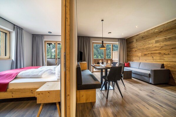 A modern room with a bed, a wooden bench, a sofa, a dining table with chairs, and a large window.