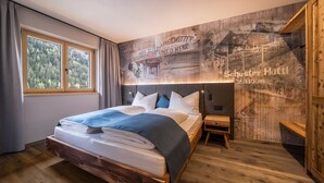 Ein modernes Schlafzimmer mit einem großen Bett, einem Nachttisch, einer Bank und Blick auf einen Wald durch das Fenster.